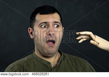 A Frightened 30-35-year-old Man Looks With Horror At A Wooden Mock-up Of An Attacking Hand. Concept: