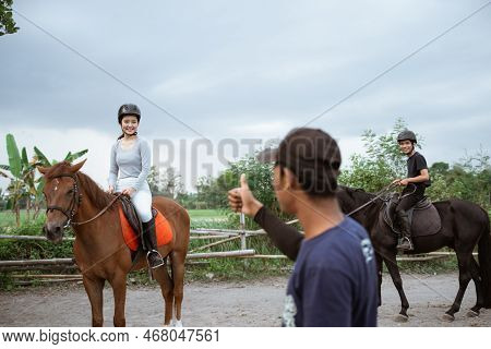 Two Equestrian Athletes Riding Horses Given Thumbs Up By Coach