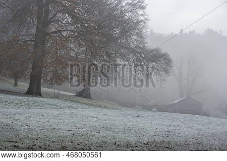 Beautiful Winter Landscape In English Countryside At Dawn With Thick Fog Hiding Farm Buildings Acros