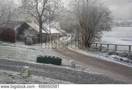 Beautiful Wintry Landscape Of Farm In Fog In English Countryside At Dawn With Hoarfrost Covering Tre