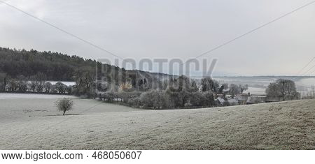 Beautiful Wintry Landscape Of Farm In Fog In English Countryside At Dawn With Hoarfrost Covering Tre