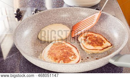 Frying Pancakes In A Frying Pan Over The Electric Stove.