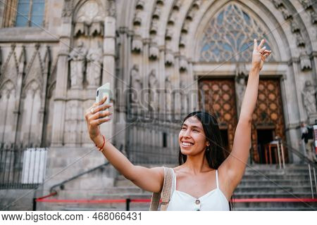 Low Angle Of Merry Latin American Woman Gesturing V Sign With Raised Hand And Smiling While Taking S