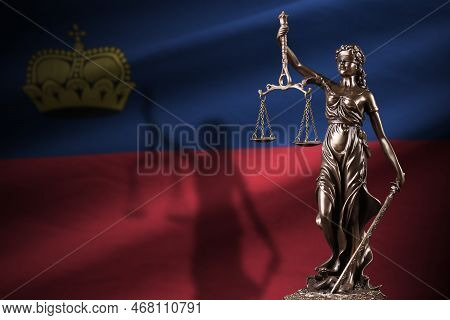 Liechtenstein Flag With Statue Of Lady Justice And Judicial Scales In Dark Room. Concept Of Judgemen