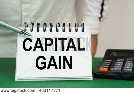 Business Concept. On A Green Surface Is A Calculator, A Man Points With A Pen To A Notebook With The