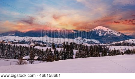 Alpine Village Outskirts Panorama In Last Evening Sunset Sun Light. Winter Snowy Hills And Fir Trees