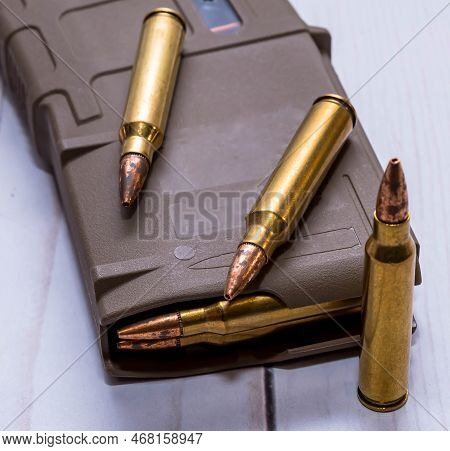 An Ar15 Rifle Magazine Loaded With 223 Caliber Bullets With Three Additional Bullets Next To It On A