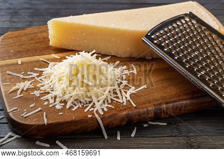 Finely Grated Parmesan Over Wooden Cutting Board. Whole And Grated Grana Padano Cheese And Stainless