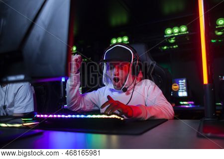 Young Emotional Guy Gamer In Headphones Sits In A Computer Club And Plays A Computer Game, A Man Scr