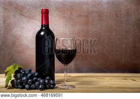 Wine Bottle And Wine Glass With Red Wine And Fresh Grapes On Wooden Table. Selective Focus.