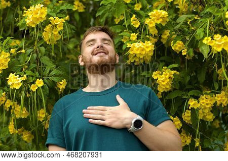 Portrait Of Happy Handsome Bearded Guy, Young Positive Man With Beard Is Smelling Beautiful Yellow F