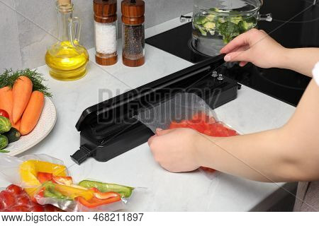 Woman Using Sealer For Vacuum Packing With Plastic Bag Of Red Pepper At White Table, Closeup