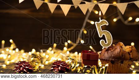 Number 5 Gold Burning Candle In A Cupcake Against Celebration Wooden Background With Lights. Birthda