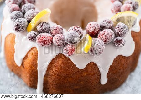 Lemon Cranberry Bundt Cake Decorated With Sugar Cranberries And Lemon Wedges On A Cake Stand.