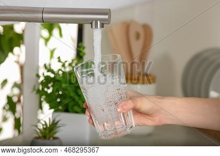 Woman Filling Glass With Tap Water From Faucet In Kitchen, Closeup