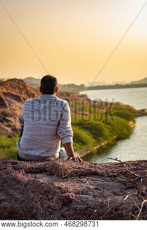 Isolated Young Man Sitting At Mountain Top With Lake View From Flat Angle