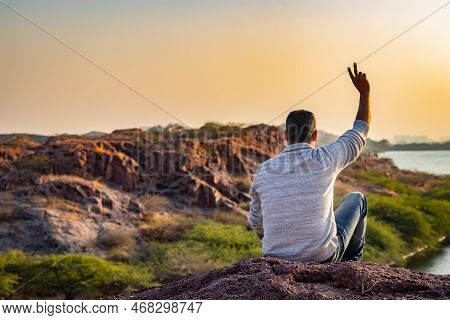 Isolated Young Man Sitting At Mountain Top With Lake View And Dramatic Sky From Flat Angle