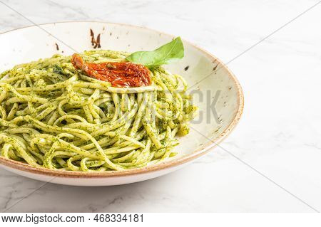 Plate Of Spaghetti With Pesto Sauce Decorated With A Sun-dried Tomato And Basilico Leaf. High Qualit