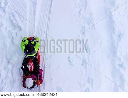 Aerial Overhead Done Photo Of Two Children In A Sled Going Down A Snow Covered Hill.