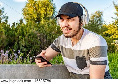 Happy Man Listening To Music With Headphones On Bench At City Park.