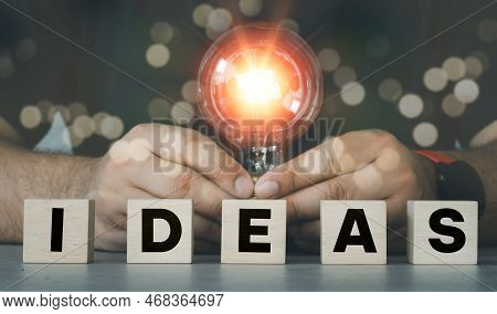 Man Hand Holding A Light Bulb With A Wood Block Word Ideas Arranged In Front, New Idea Concept With 