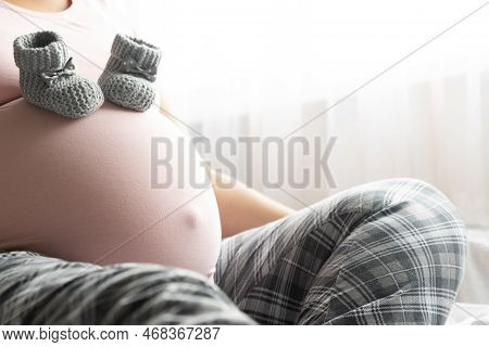 Two Little Wool Booties On Belly Of Pregnant Woman. Healthy Pregnacy.