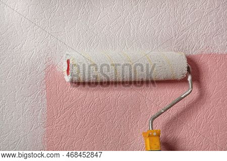 An Old, Fuzzy Paint Roller Draws Pink Wallpaper On The Wall With White Paint. Copy Space.