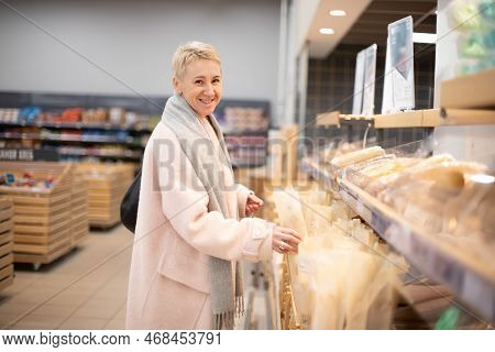 Smiling Senior Mature Woman Choosing Bread And Baking In Grocery Section Of Supermarket At The Baker