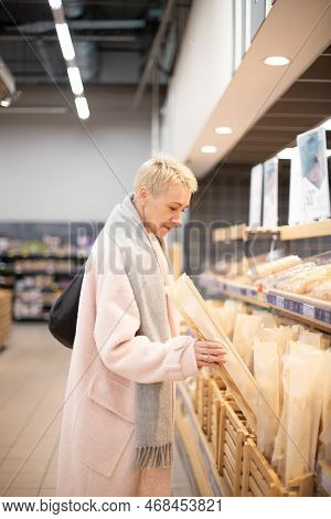 Smiling Senior Mature Woman Choosing Bread And Baking In Grocery Section Of Supermarket At The Baker