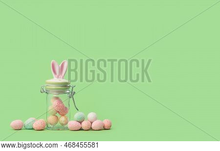 Easter Bunny Ears Sweets Jar With Many Tiny Eggs In And Near On Green Edgeless Background. Happy Eas