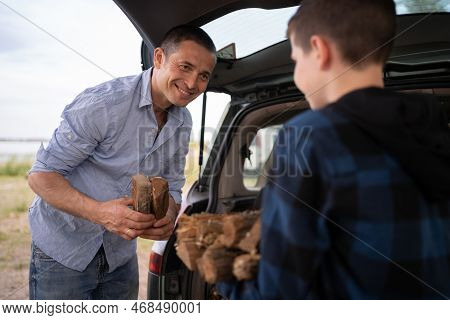 Father's Day In Nature. Son And Father Getting Firewood From The Car For The Campfire. Happy Family 