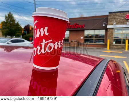 Oshawa, Canada - 19 October 2022: Cup Of Tim Hortons Coffee On Red Car In Front Of Outlet With Logo