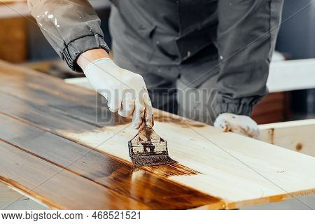 Man Paints Wooden Boards With Paint Brush. Carpenter Cabinetmaker Varnishes Wooden Surface. Authenti