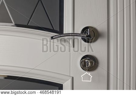 The Concept Of Buying A New House. A Key With A Key Fob In The Shape Of A House In A Door Lock. Real