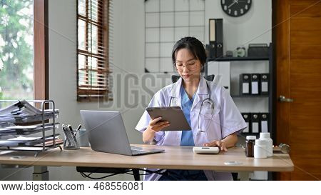 Beautiful Asian Female Doctor Using Calculator And Digital Tablet, Working In The Office.