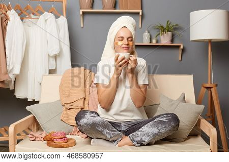 Indoor Shot Of Joyful Relxed Woman Wearing Home Clothes And With Towel On Head Sitting On Sofa With 