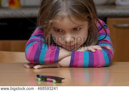 A Little Girl Looks At A Fingerboard On A Wooden Table, Close-up, Selective Focus.finger Training.