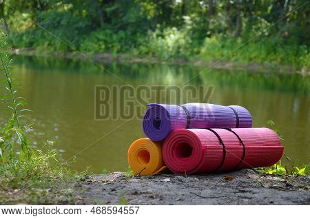 Yoga, Fitness Or Tourist Mats On The Green Grass Outdoors Close To River And Forest. Mat For Sports 