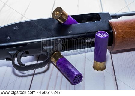A 12 Gauge Shotgun With An Opened Chamber And Three Shells On White Wooden Background