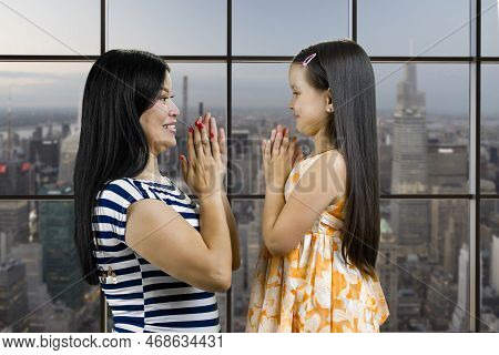 Side View Of A Young Mother And Her Daughter Are Playing Clapping Game. Checkered Window Background 