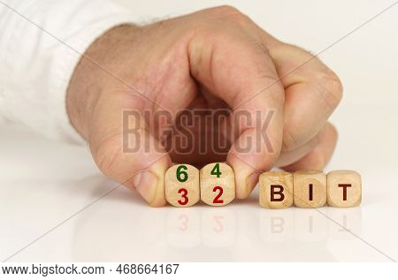 On A Reflective White Surface In The Hands Of A Man Are Cubes With The Inscription - 64 Bit Or 32 Bi