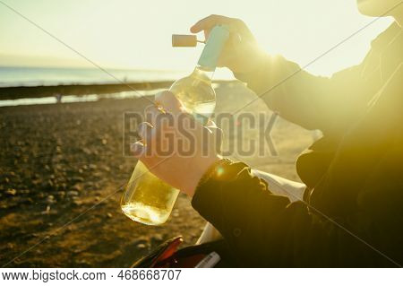 A Man On The Shore Of The Sea Or Ocean Opens A Bottle Of White Wine. A Date On The Beach, Alcohol On