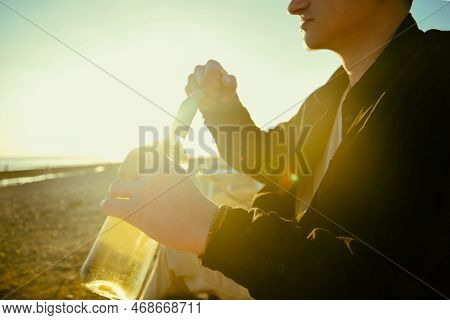 A Man On The Shore Of The Sea Or Ocean Opens A Bottle Of White Wine. A Date On The Beach, Alcohol On
