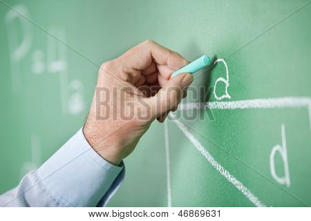Closeup ของครูผู้ใหญ่มือเขียนอักษรบน greenboard ในห้องเรียน