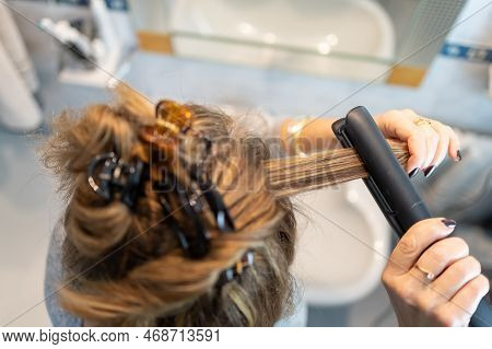 Blonde Woman Ironing Her Hair With An Electrical Appliance In The Bathroom, Top View.