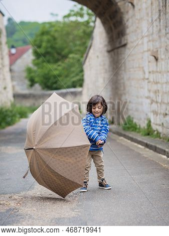 Little Handsome Baby Boy Playing With Umbrella Outdoor In Old Town. Boy Wearing Blue Jacket
