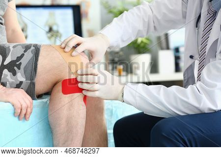 Physiotherapist Applying Kinesiotape To Patient Knee In Clinic Closeup. Injury And Sprain Of Knee Jo