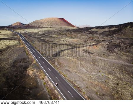 A Cyclist Rides Along A Road Among Volcanic Craters, Lanzarote Island, Spain.