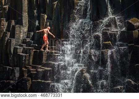 Caucasian Man In Swimsuit Balancing Near The Falling Water Streams Flowing On Black Volcanic Stone C
