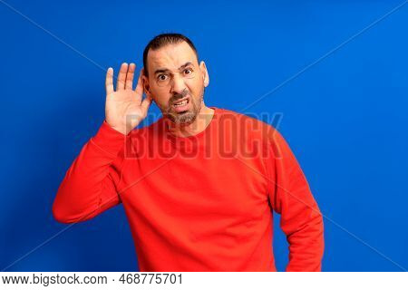 Listening Man Holds His Hand Near His Ear On A Blue Background. Handsome Man Trying To Listen To Som